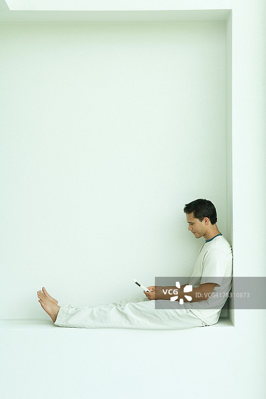 男人坐在窗台上用手机，全身，侧视图图片素材