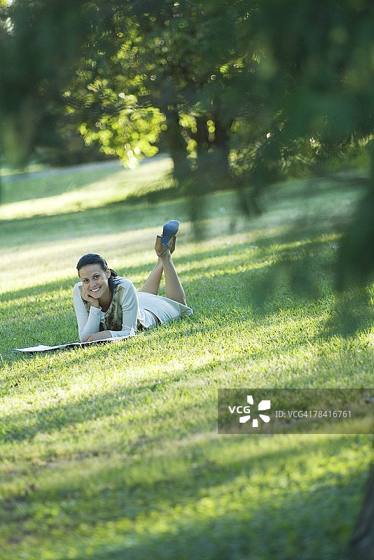 年轻女子躺在草地上，对着镜头微笑图片素材