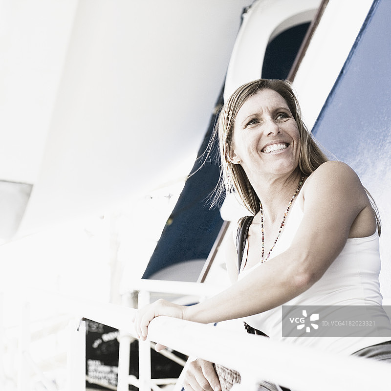 一位中年妇女微笑着站在一艘游轮的楼梯上的侧影图片素材