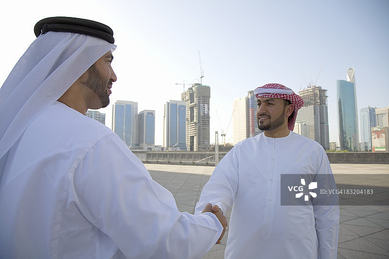 两名身着传统中东服饰的男子在阿联酋迪拜城市的背景下相互问候图片素材
