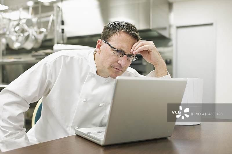 沮丧的厨师看着厨房里的笔记本电脑图片素材