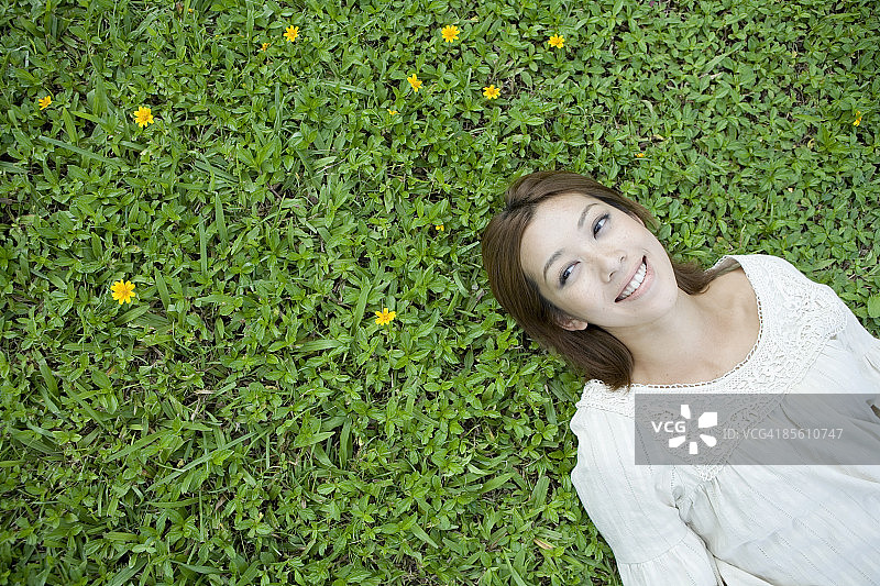 年轻女子仰面躺在草地上，面带微笑图片素材
