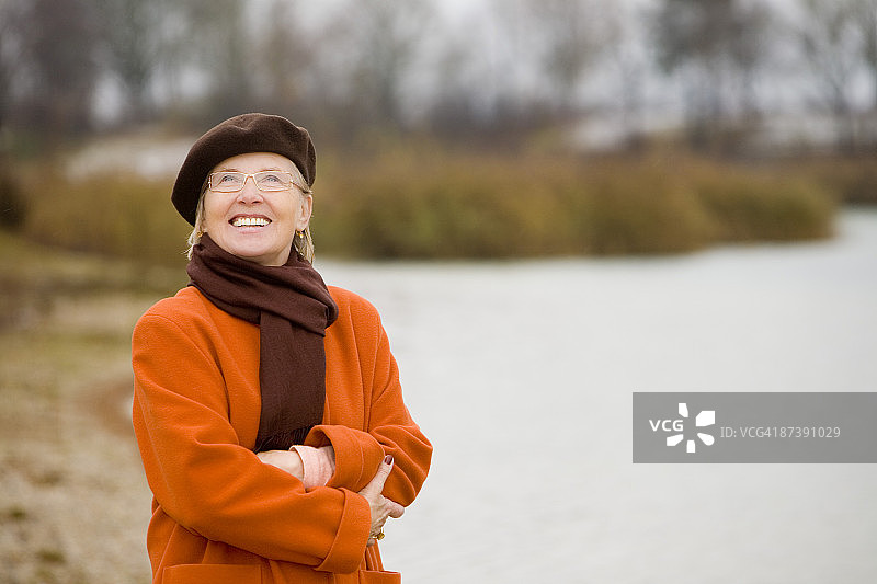 戴着棕色贝雷帽站在公园湖边的成熟女人的肖像图片素材