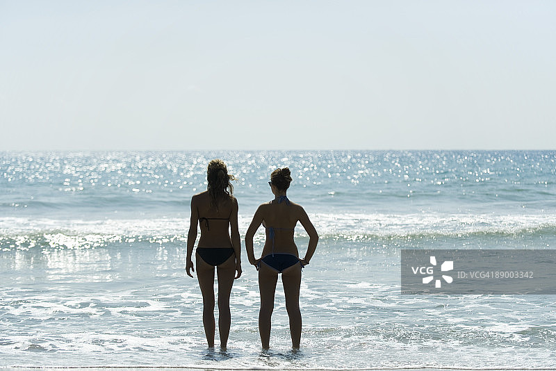 十几岁的女孩肩并肩站在沙滩上，望着地平线图片素材