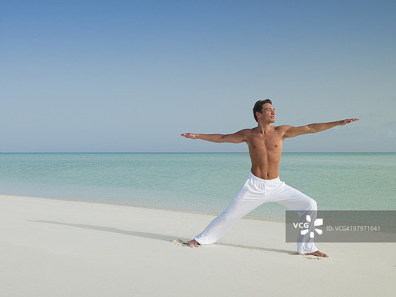 穿着武士瑜伽的男人在海滩上摆姿势图片素材