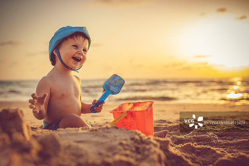 快乐的小男孩在日落的海滩上建造沙堡图片素材