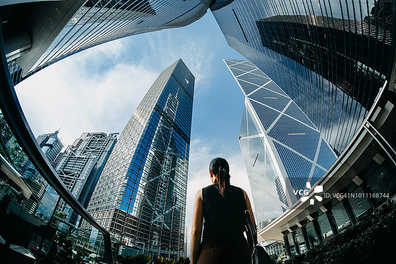 后视图专业的年轻女商人站在市中心金融区的现代金融摩天大楼，以积极的情绪仰望天空图片素材