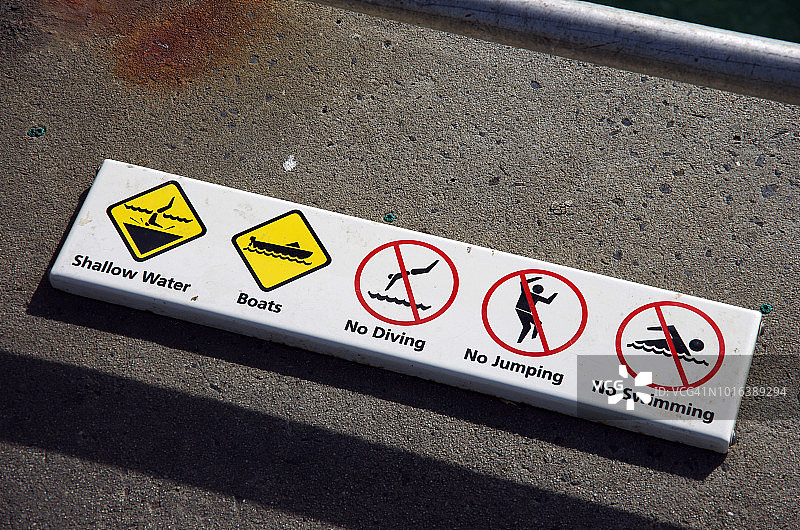 在码头边缘张贴“浅水”、“船只”、“禁止潜水”、“禁止跳跃”及“禁止游泳”的安全警告标志图片素材