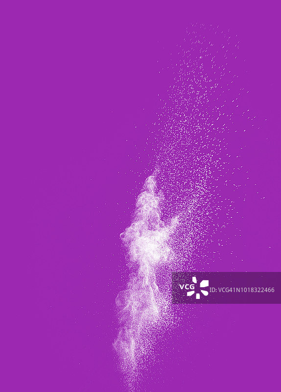 由一团白色粉末颗粒在紫罗兰色背景上撞击而成的爆炸。图片素材