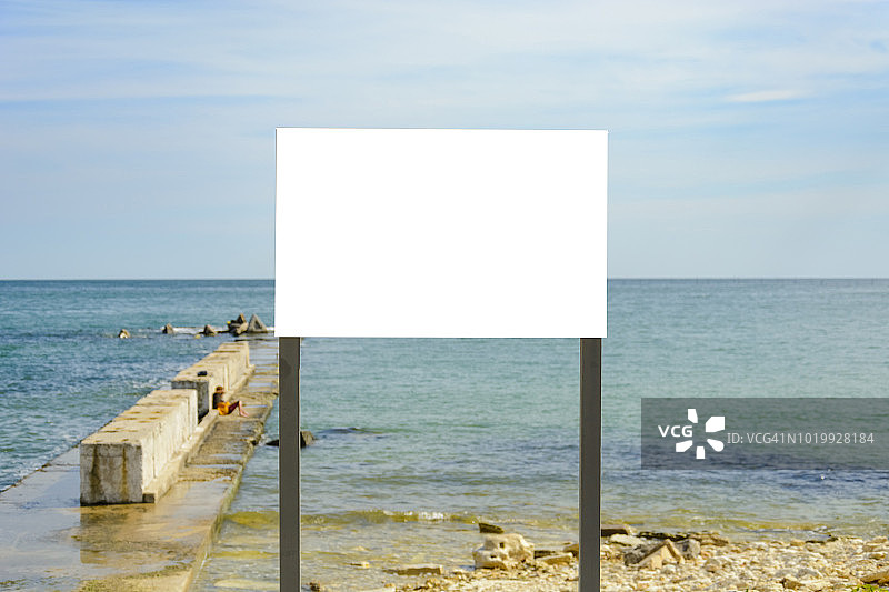 海滩上的空白标志对着海水和码头。图片素材