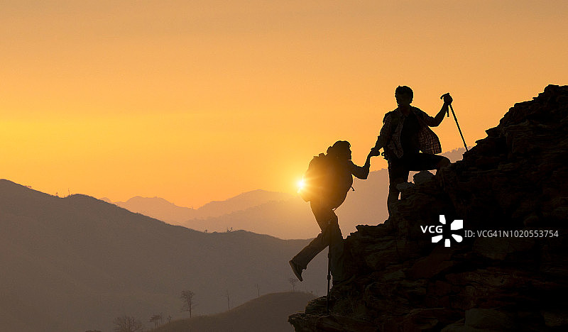 日出时，人们互相帮助爬山。伸出援手，积极健康的生活方式理念。图片素材