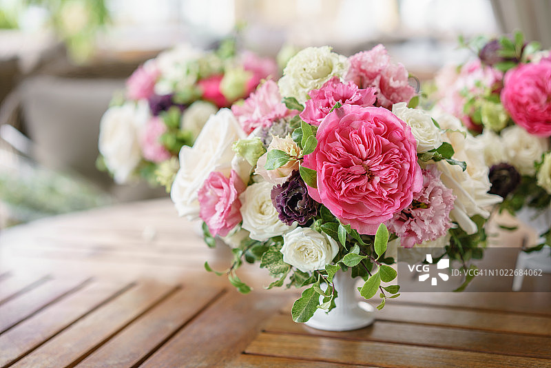 用柔和的颜色排列鲜花。婚礼的背景。餐厅的餐桌。不同品种的花园和灌木玫瑰在一个轻花瓶上的木桌图片素材