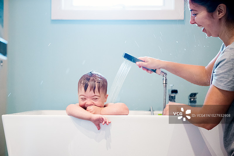 唐氏综合症的小男孩在洗澡，妈妈在给他洗澡。图片素材