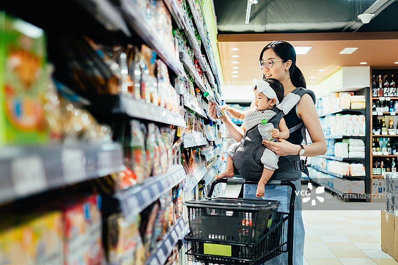 年轻妈妈带着女儿在超市购物，选择有机婴儿食品，阅读营养标签图片素材