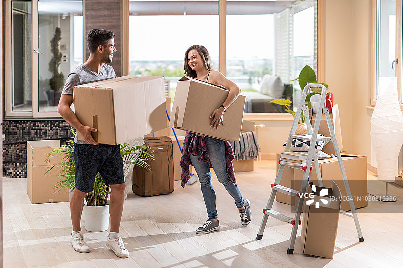 在他们的新公寓里，一对年轻幸福的夫妇一边拿着纸板箱一边交流。图片素材