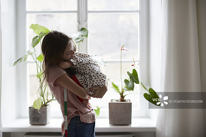 侧面的时装设计师拥抱女儿，而站在家里图片素材
