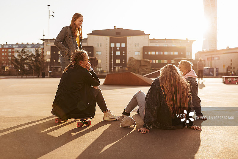 十几岁的女孩坐在滑板上，而与朋友在公园在阳光明媚的一天图片素材