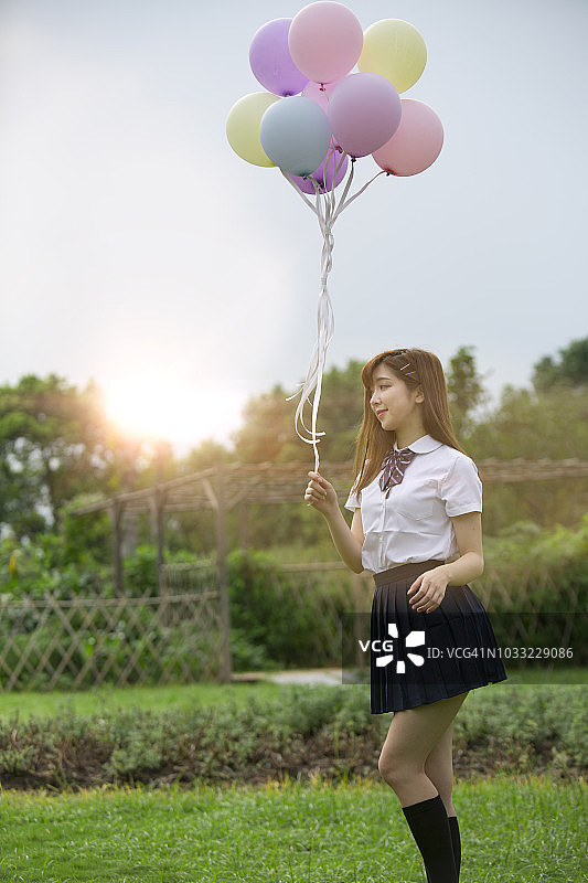 夏天五颜六色的气球。年轻的成年亚洲女孩举着一束彩色气球站在公园里的肖像。图片素材