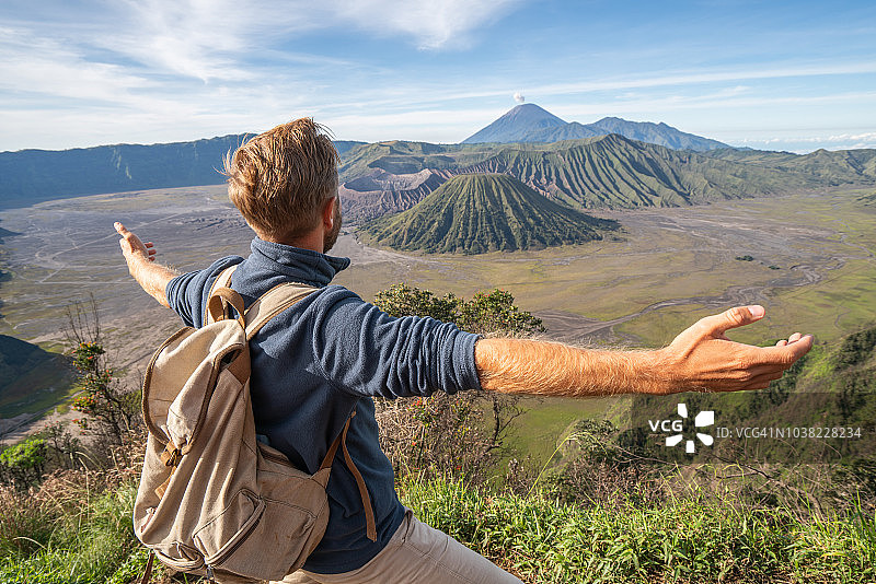 在印度尼西亚，年轻人徒步旅行，手臂伸开站在火山的山顶上，人们旅行的乐趣，冒险的概念，成功和成就图片素材