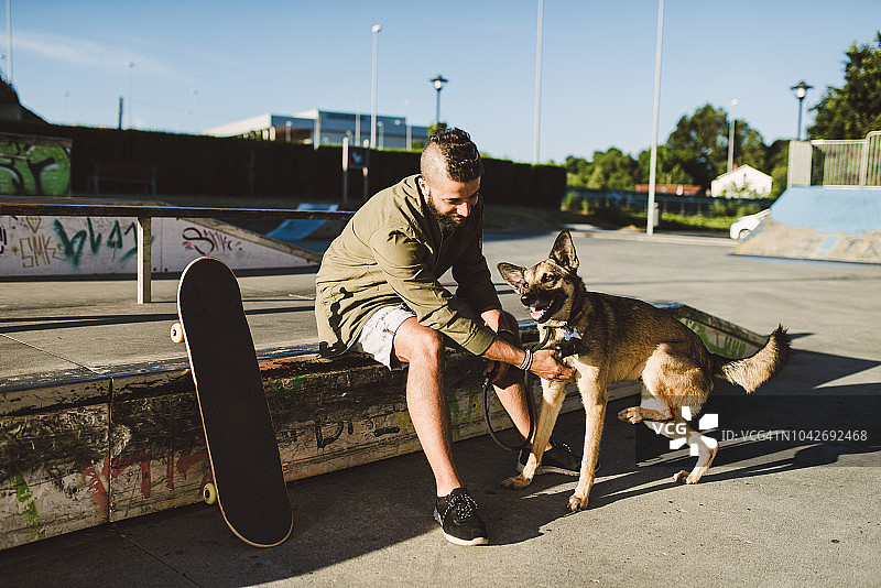 一个年轻人和他的狗在滑板公园玩图片素材