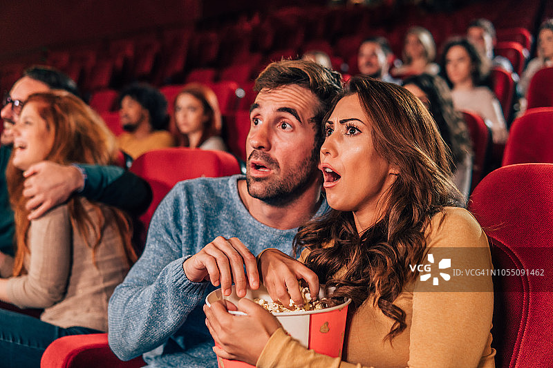 一对吓坏了的夫妇在电影院吃爆米花图片素材