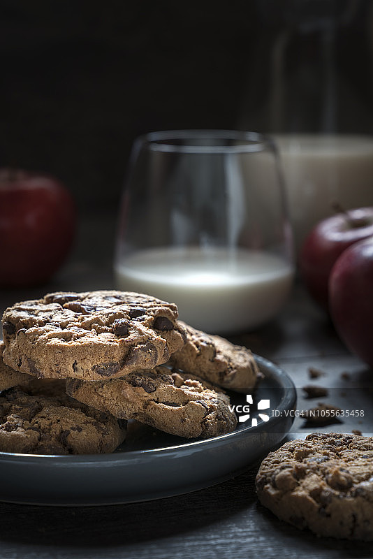 巧克力饼干，牛奶杯和苹果在深色的木头背景。图片素材