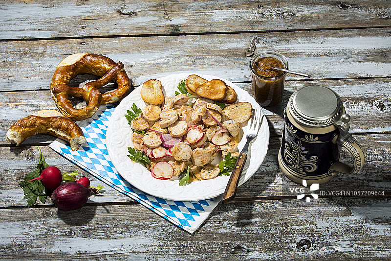 巴伐利亚小牛肉香肠沙拉配烤椒盐卷饼，甜芥末，椒盐卷饼，红萝卜和啤酒杯图片素材