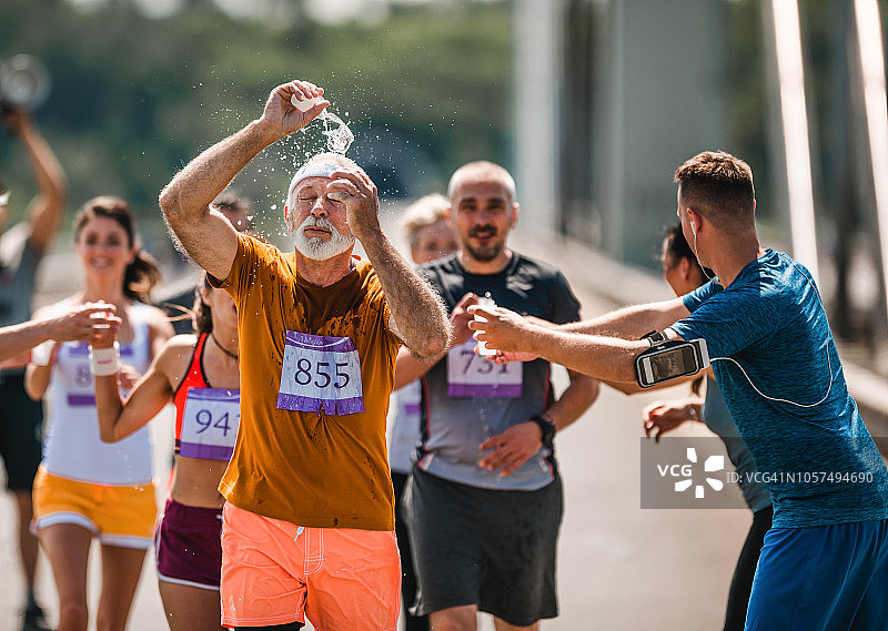 老人在路上跑马拉松，喝点水提神。图片素材