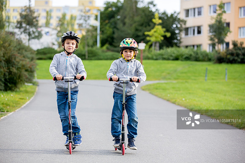 两个孩子，兄弟，在一个阳光明媚的秋日在公园里骑摩托车图片素材
