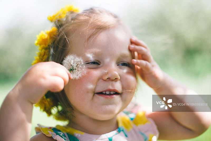 一个微笑的年轻女孩的肖像，抚摸着她的头，手里拿着蒲公英在春天图片素材