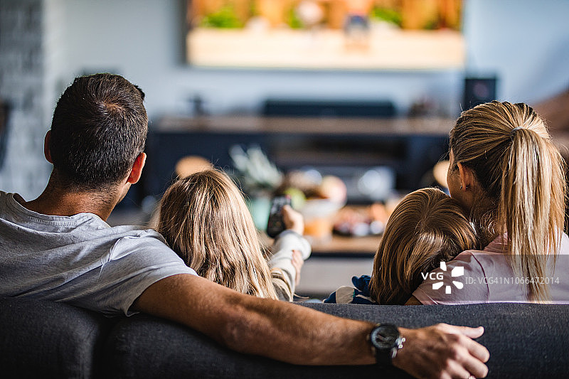 一个家庭在家里的沙发上看电视的后视图。图片素材