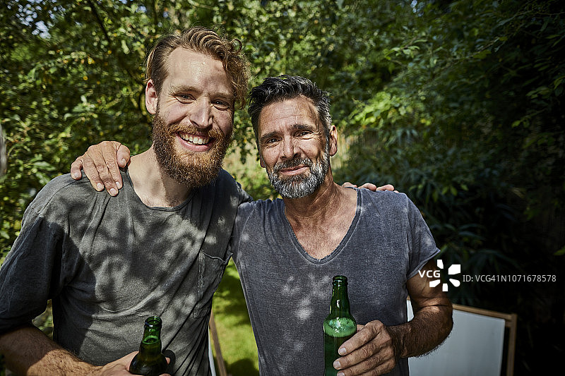两个微笑的男人在花园里抱着啤酒瓶的照片图片素材