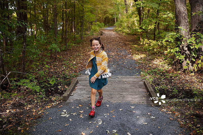 美国，一个女孩在森林小径上跑过一座小桥图片素材