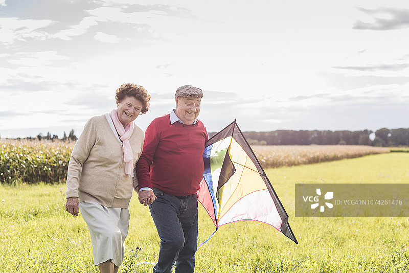 一对快乐的老年夫妇带着风筝在乡村风景中散步图片素材