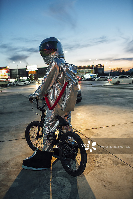 宇航员晚上在城市的停车场上骑着小轮车图片素材