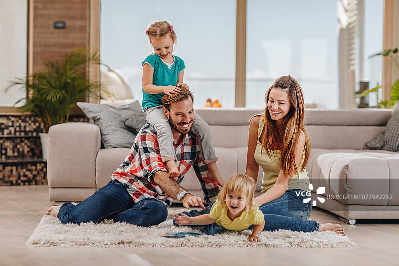 年轻快乐的家庭在客厅的地毯上玩耍。图片素材