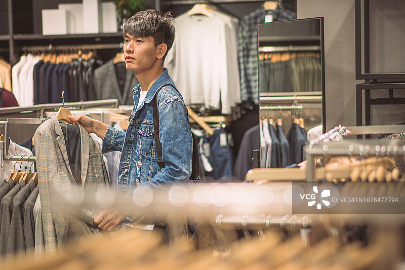 快乐的年轻亚洲男人在购物中心或服装店选择夹克图片素材
