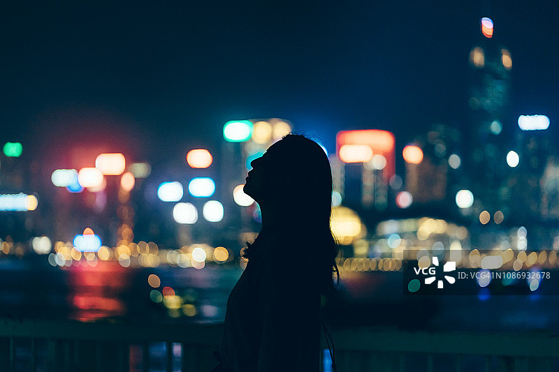 女人的剪影放松和仰望天空的灯光和多色的城市景观在晚上图片素材