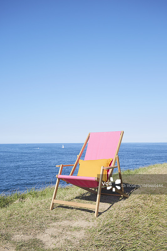 在海边的草地上，蓝色的天空映衬着粉红色的靠背躺椅图片素材