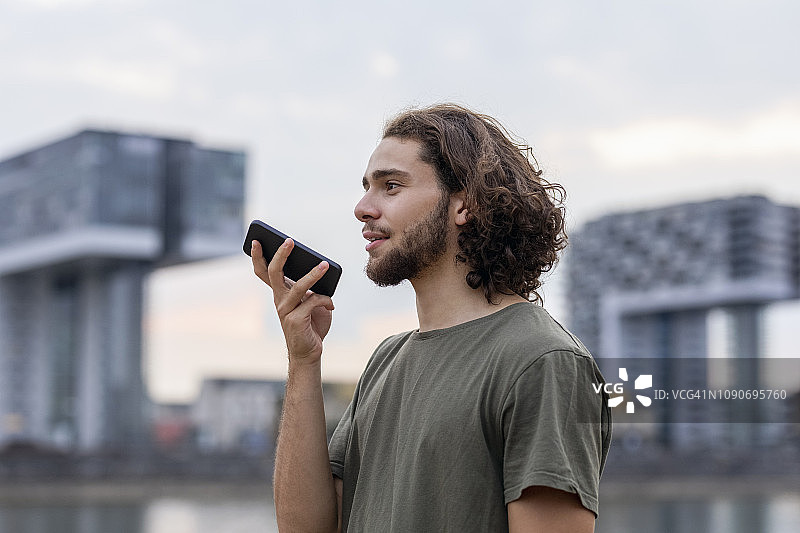 德国，科隆，一个年轻人在河边使用智能手机图片素材