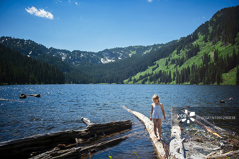 在森林的蓝天下，女孩在湖上的原木上行走图片素材