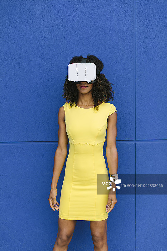 穿着黄色衣服戴着蓝色背景的虚拟现实眼镜的女人图片素材