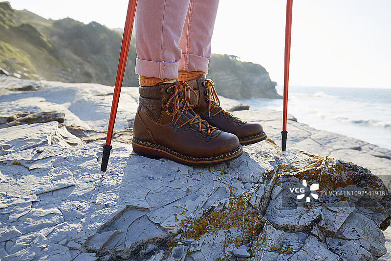 穿着登山靴的女人站在海边的岩石上图片素材