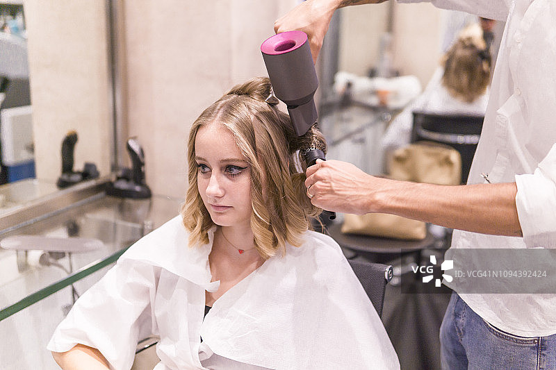 男士发型师在美容院为十几岁的顾客烘干头发图片素材