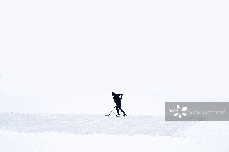 一个年轻人在结冰的湖面上练习冰球。图片素材