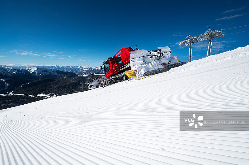 现代的红色雪清理过剩的雪在一个美丽的，阳光明媚的日子在山上滑雪道的下坡图片素材