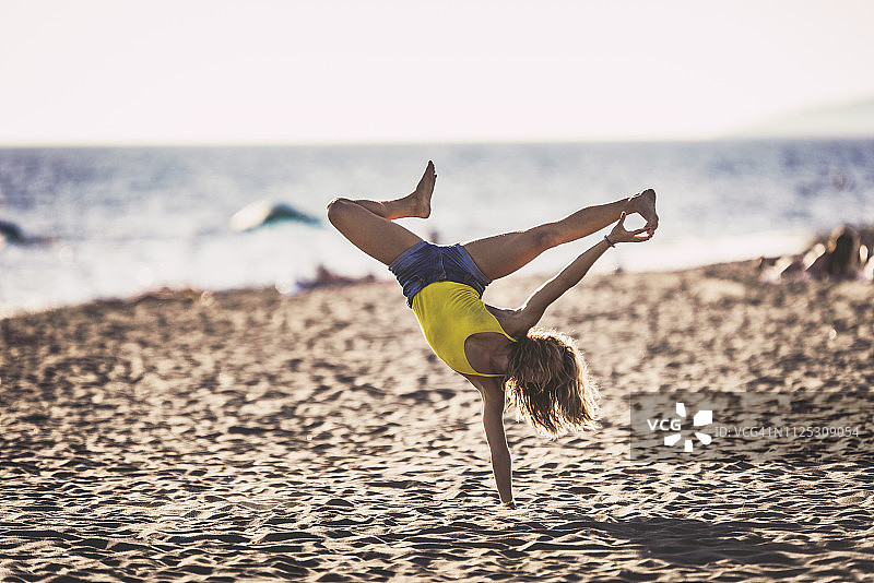 一个女人的全身在沙滩上做倒立。图片素材