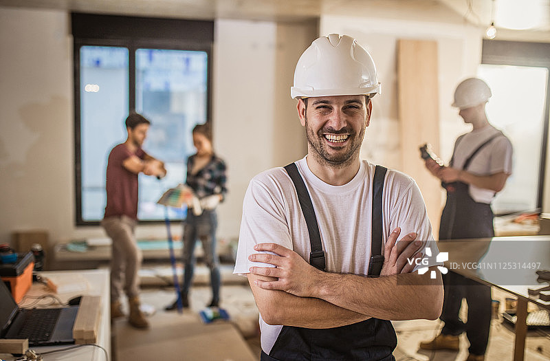 快乐的工人站在建筑工地，双臂交叉，看着镜头。图片素材