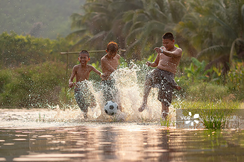 亚洲儿童在河中踢足球，足球运动员在日落的河上行动。图片素材