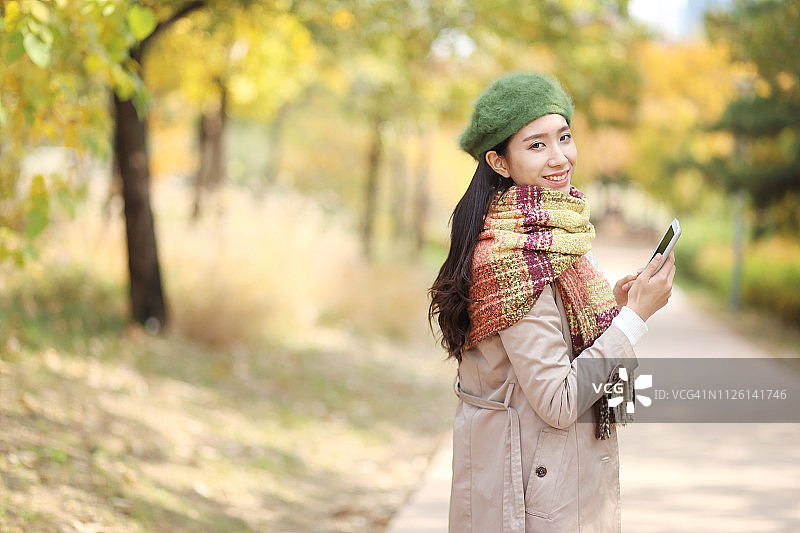 在秋天公园里拿着智能手机的年轻女子图片素材